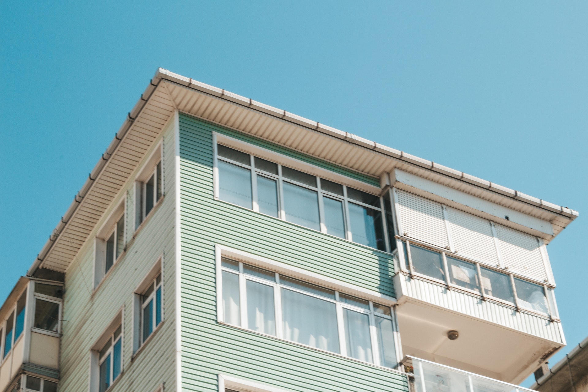 Blick auf ein Mehrfamilienhaus, welches mit grünem Holz verkleidet ist und große Fensterfronten hat. Die Wohnungen scheinen alle bewohnt. Auch für solche Objekte muss der Wert der Immobilie festgestellt werden.